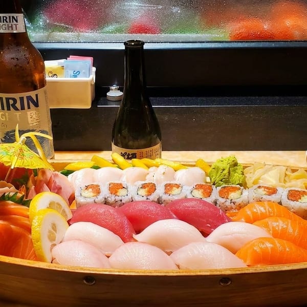 A large wooden boat filled with an assortment of sushi, sashimi, and rolls, with beer and sake.