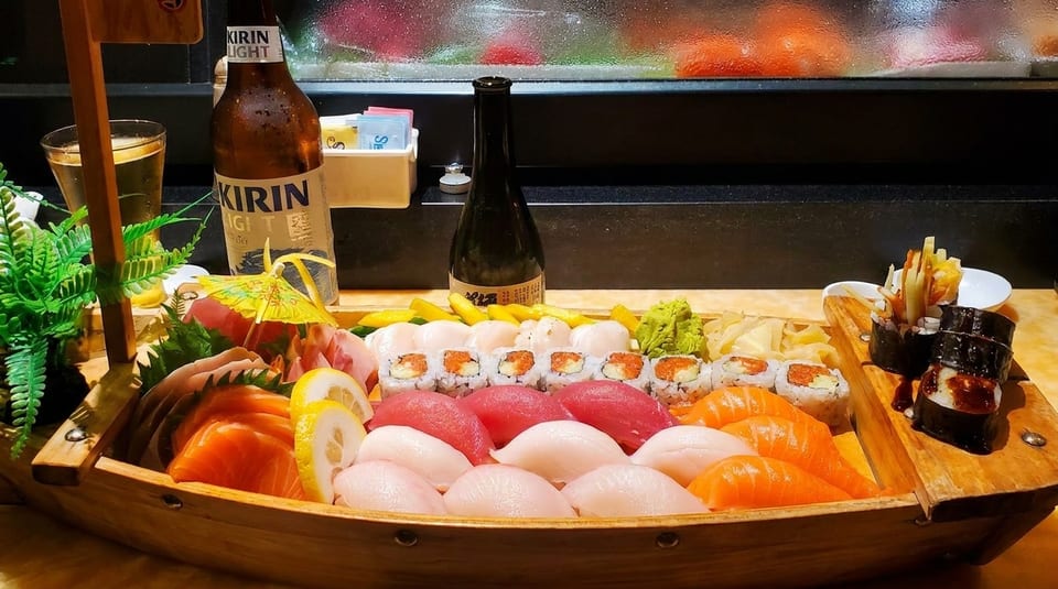 A large wooden boat filled with an assortment of sushi, sashimi, and rolls, with beer and sake.