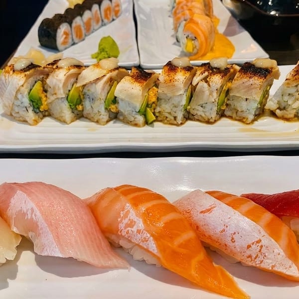 Plates of various sushi rolls and nigiri, including salmon, tuna, and yellowtail, on a dark table.