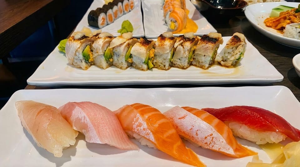 Plates of various sushi rolls and nigiri, including salmon, tuna, and yellowtail, on a dark table.